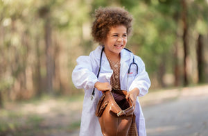 A little girl holds open her doctor bag while wearing a lab coat and stethoscope